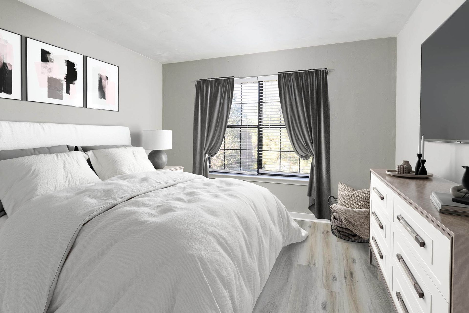 Modern apartment bedroom with white bedding, gray walls, large window with curtains, and dresser.