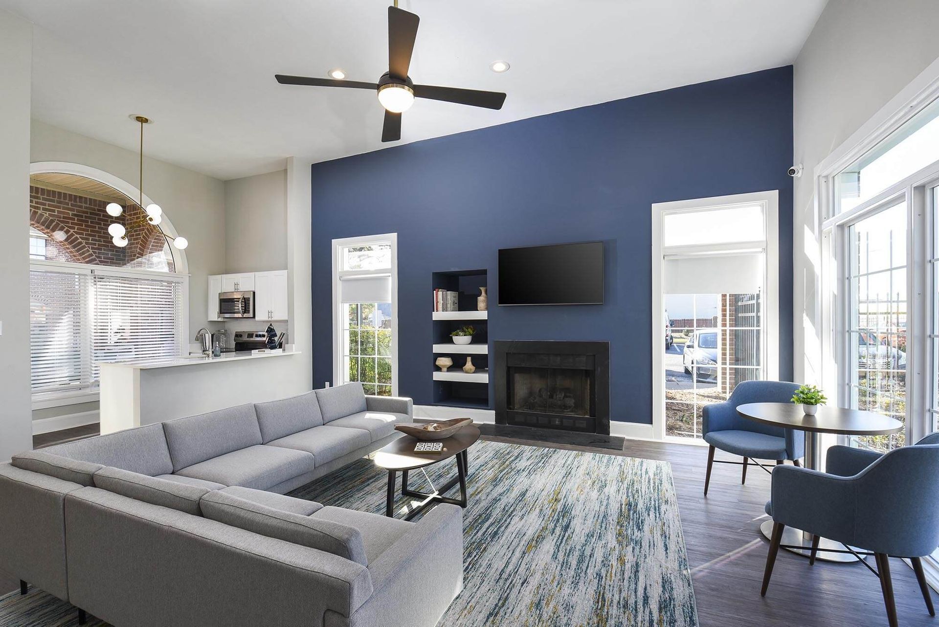 Modern living room in a multifamily unit with a gray sectional, blue accent wall, fireplace, and open kitchen.
