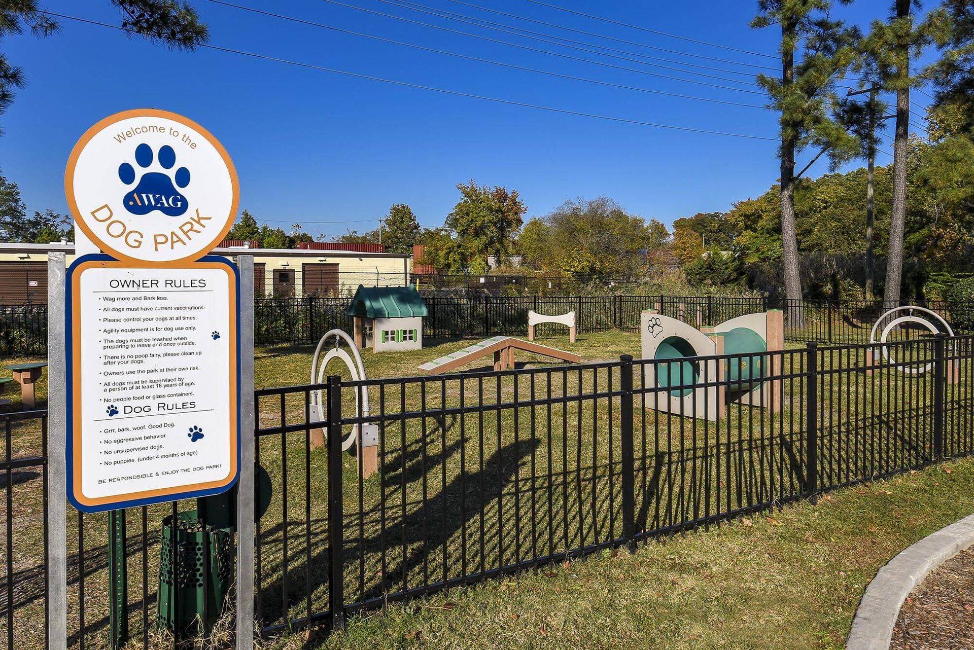 Fenced dog park with a large Welcome to the Dog Park sign and small play structures.