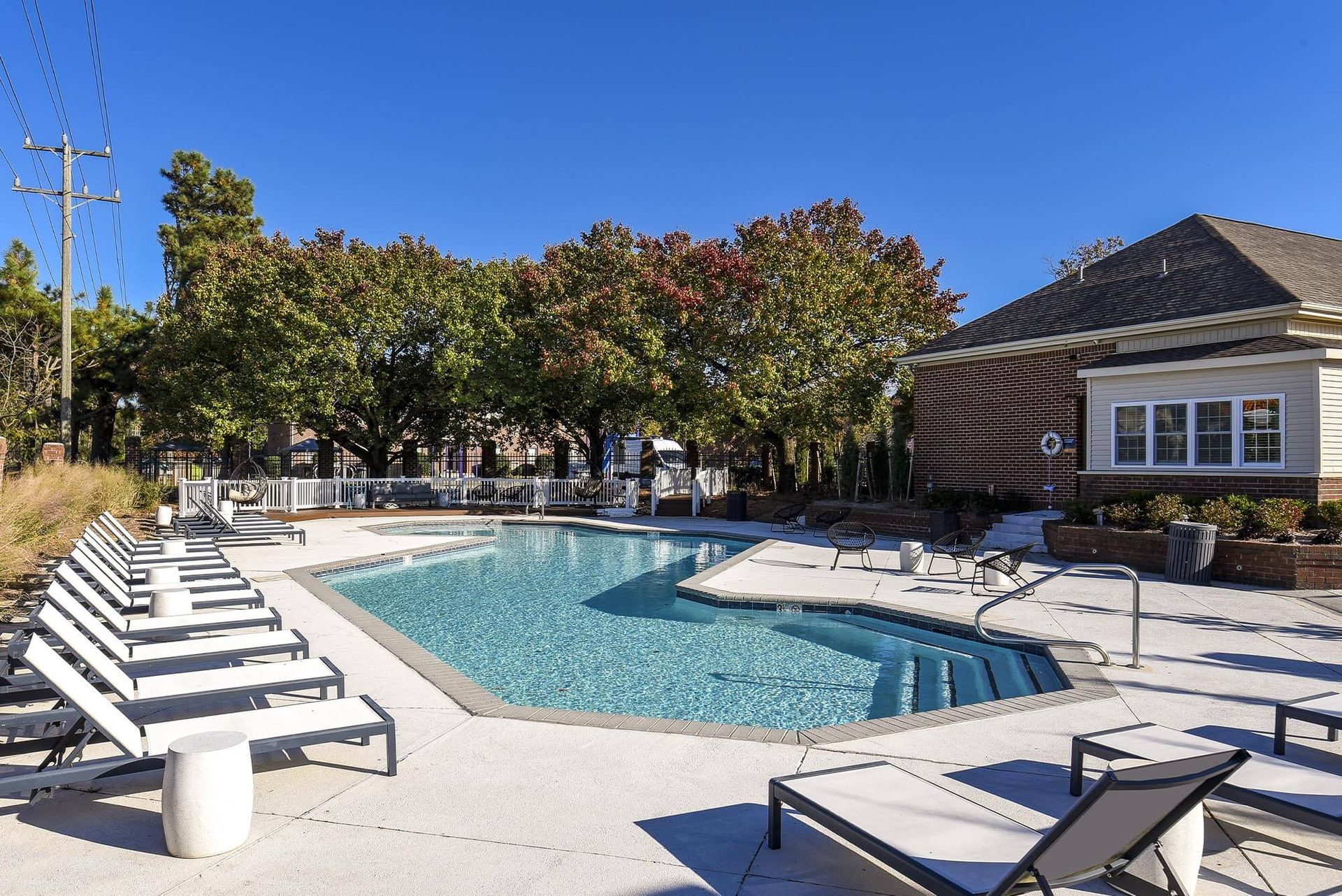 Outdoor apartment community pool with lounge chairs, clear water, and surrounding trees.