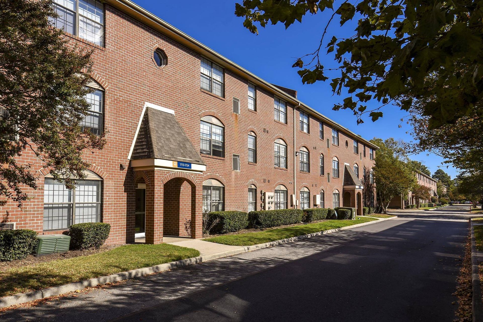 Exterior view of a brick apartment building with arched windows along a tree-lined street.