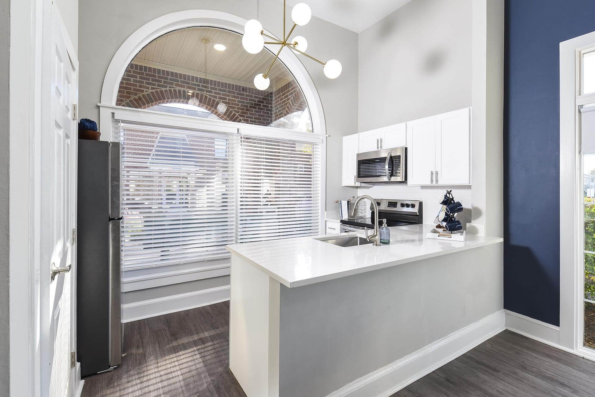 Bright kitchen with white cabinets, island, stainless appliances, and a large arched window with blinds.