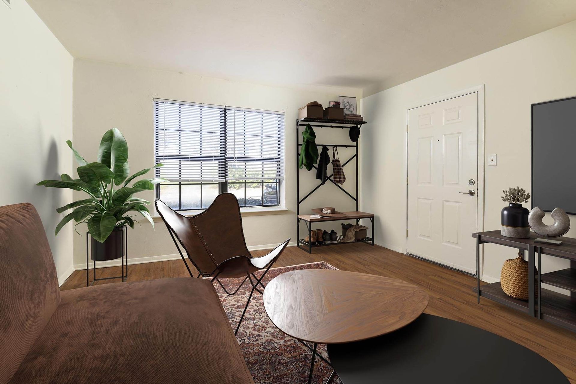 Living room of an apartment with sofa, sling chair, coffee tables, plant, and coat rack near a window.