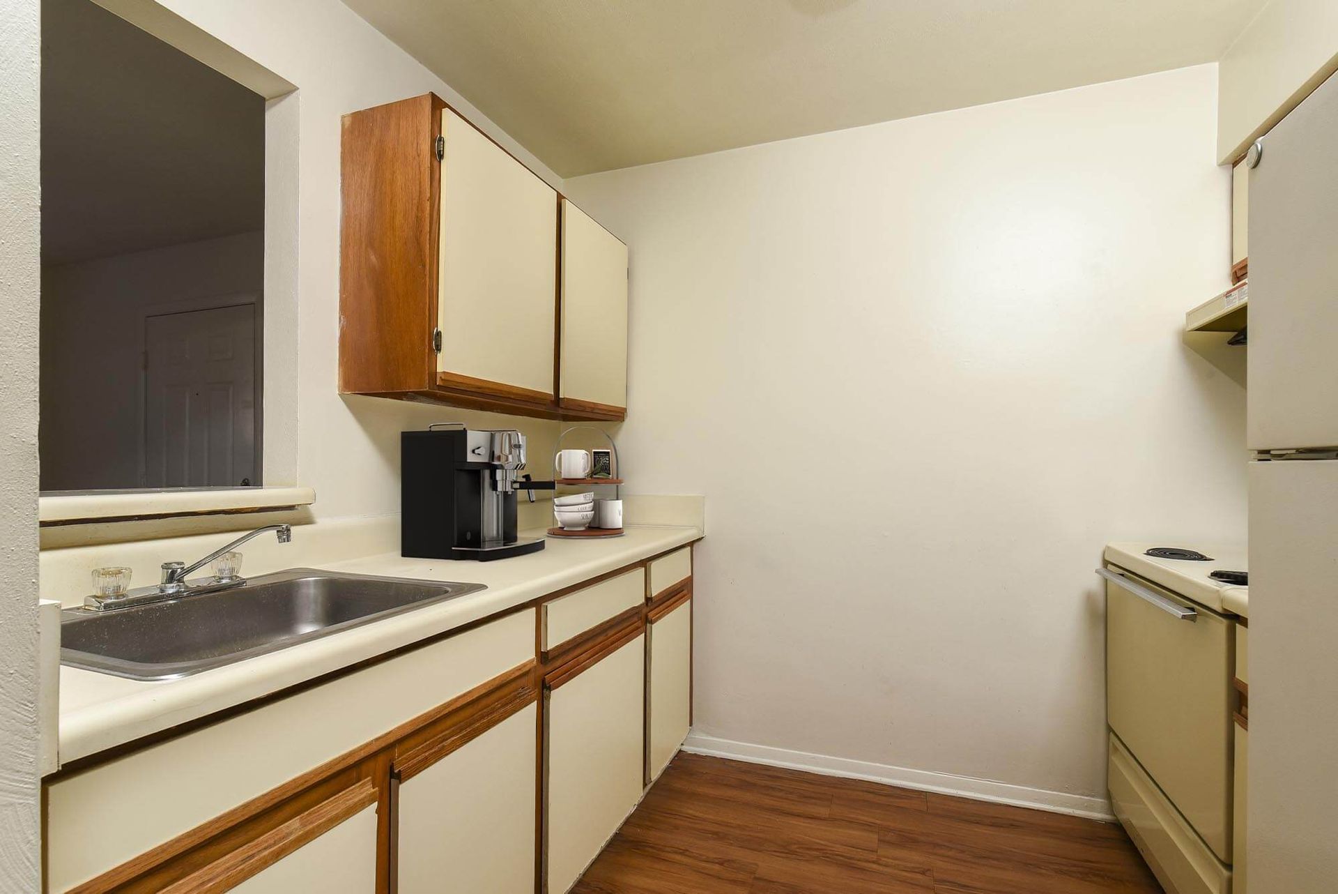 Galley-style apartment kitchen with a double sink, upper cabinets, and appliances.