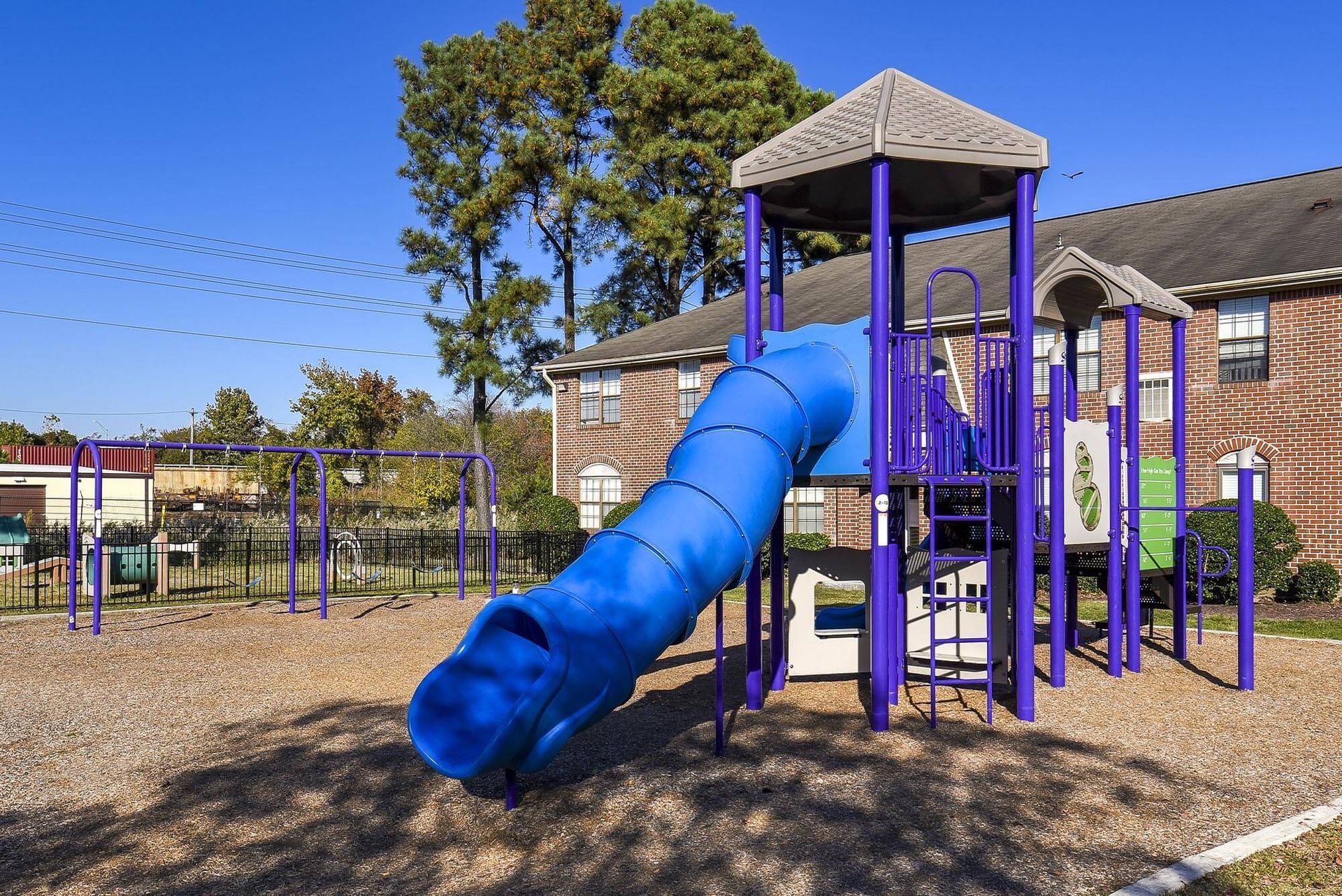 Bright playground with a long blue tube slide and purple climbing structures in a residential yard.