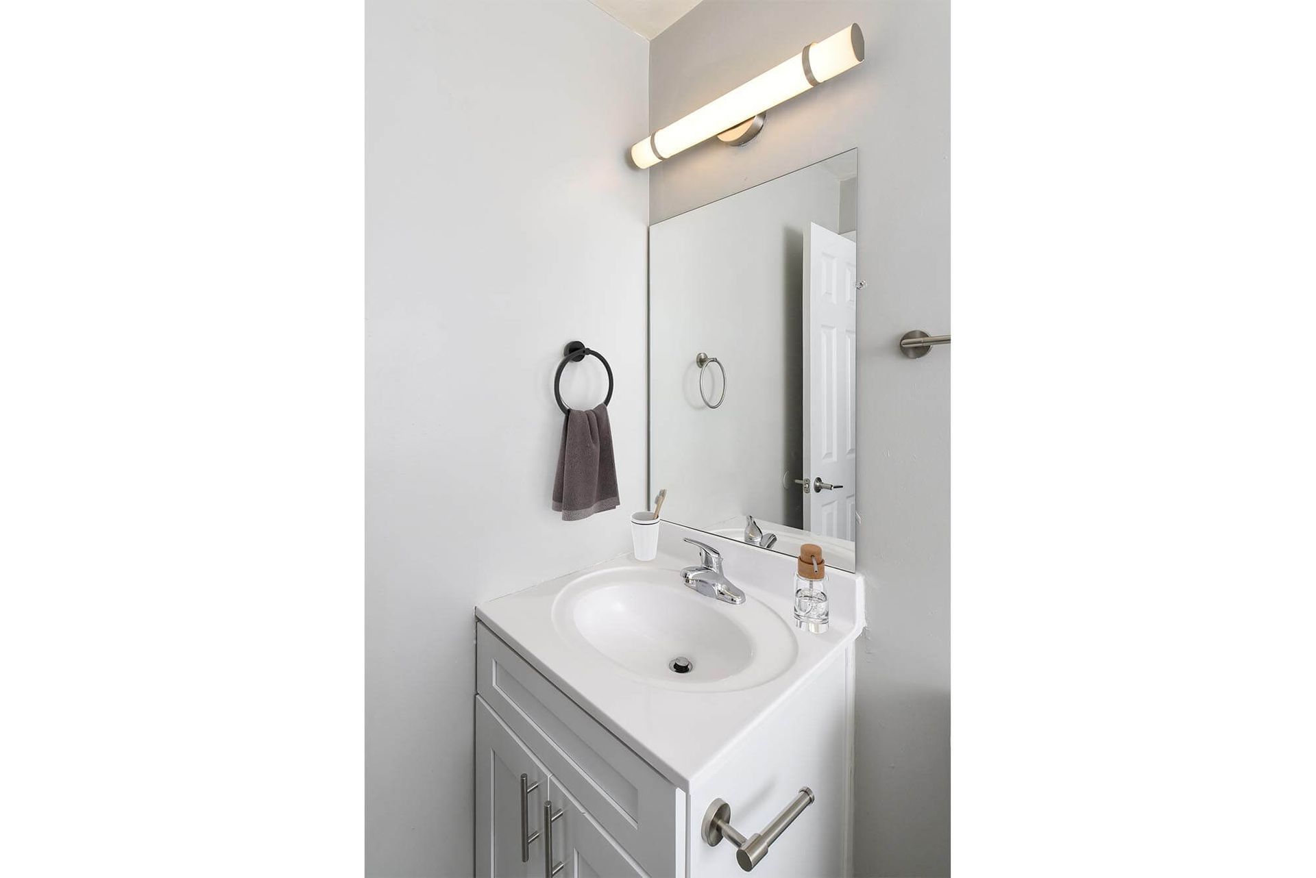Bathroom vanity with white sink, mirror, towel ring, and brushed metal fixtures.