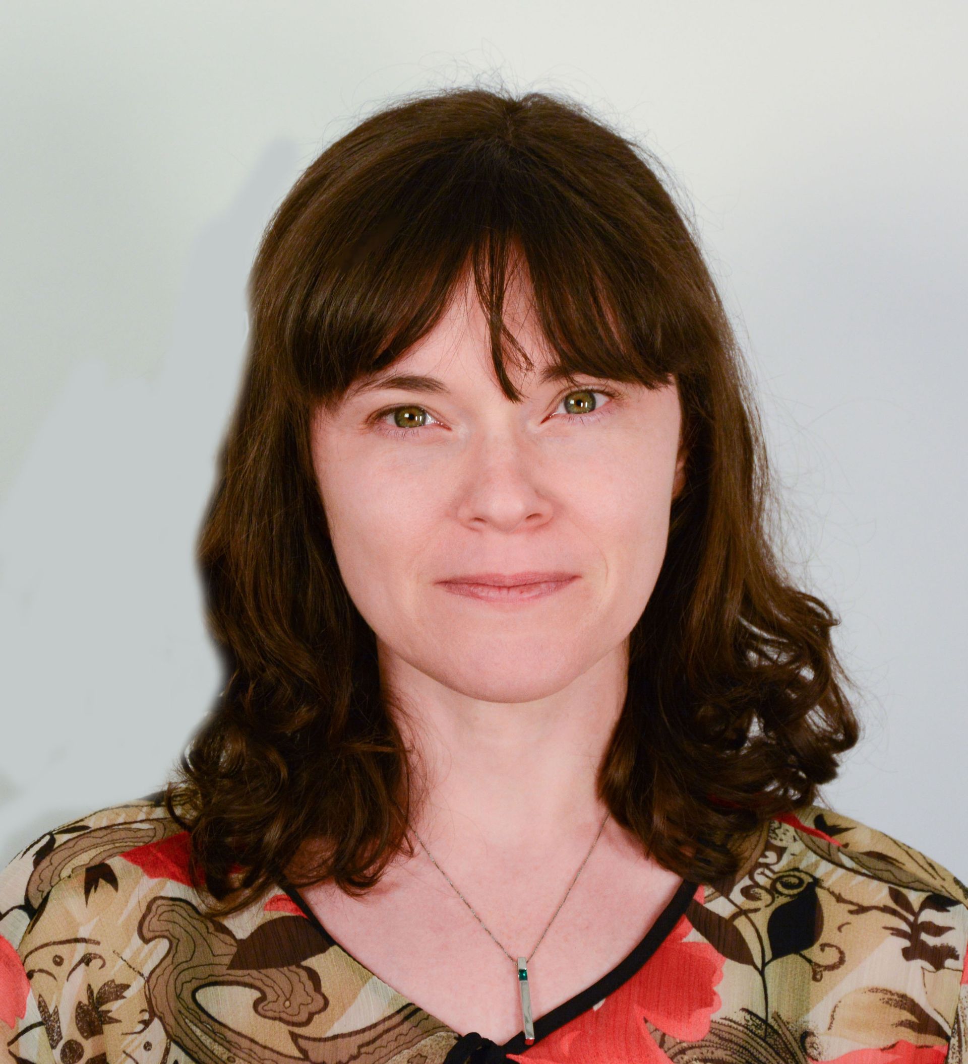 Woman with brown hair and bangs, wearing a floral top, looking at the viewer.