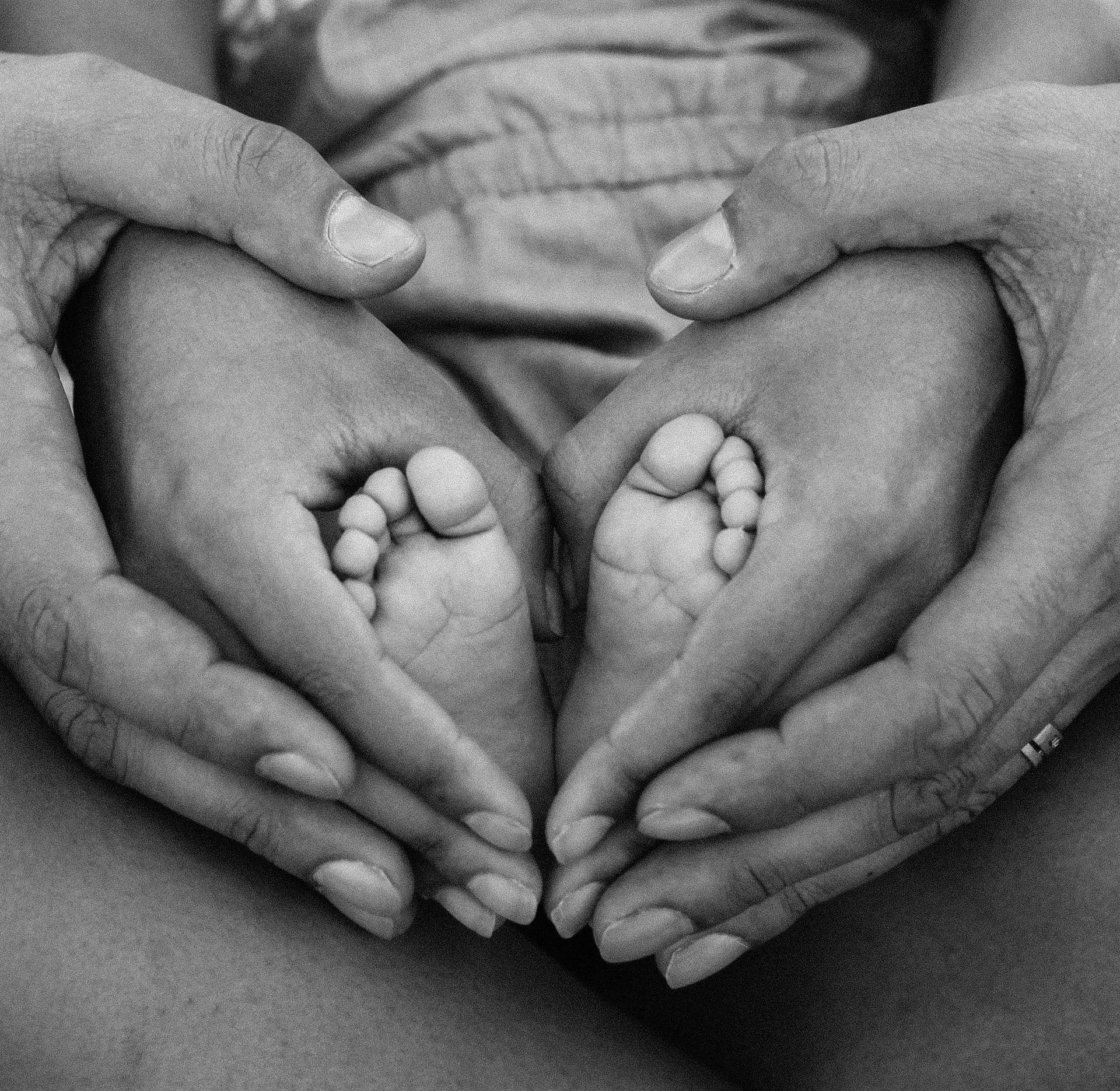 Adult hands cradling a baby's feet, forming a heart shape, in black and white.