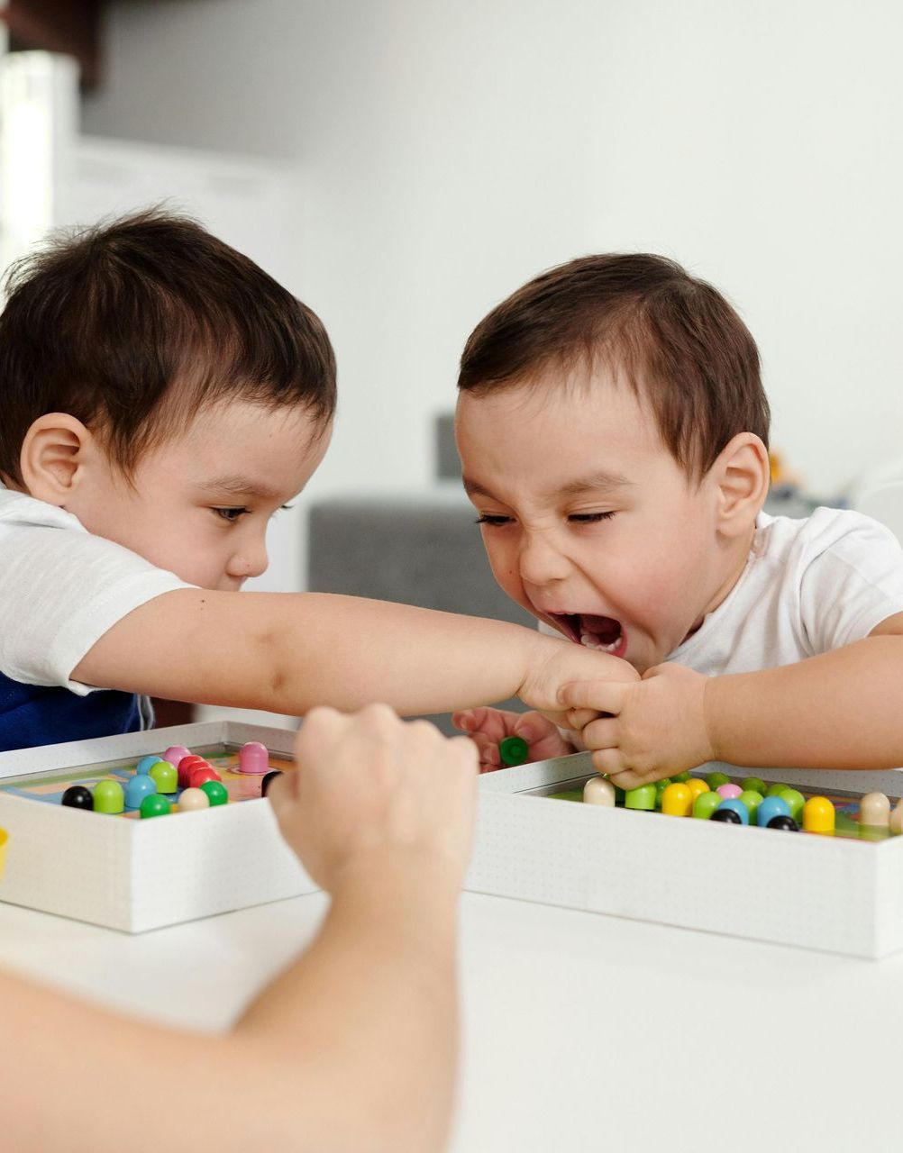 Two toddlers fighting over a toy, one crying, at a table.