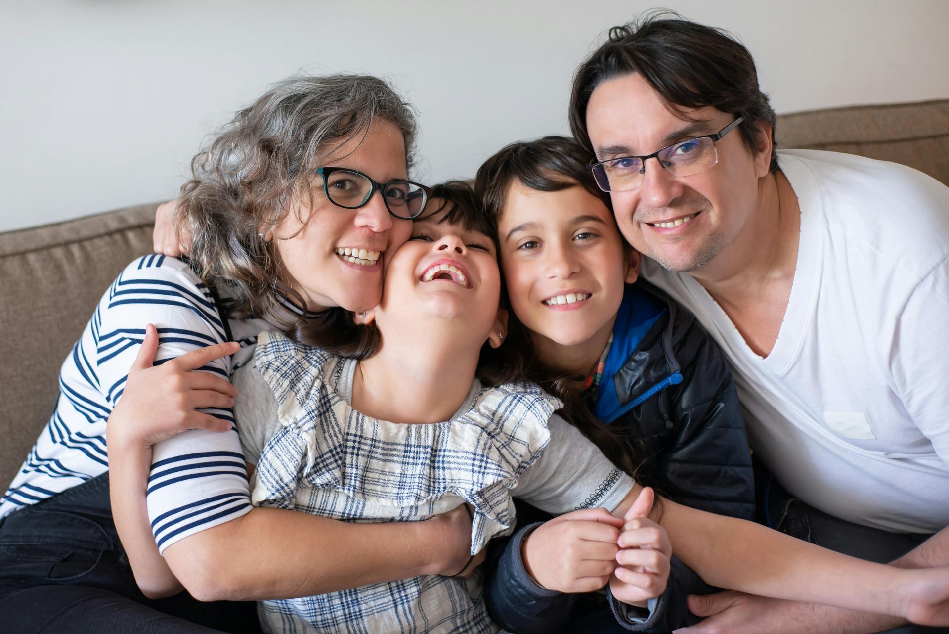 Family of four smiling and embracing on a couch.