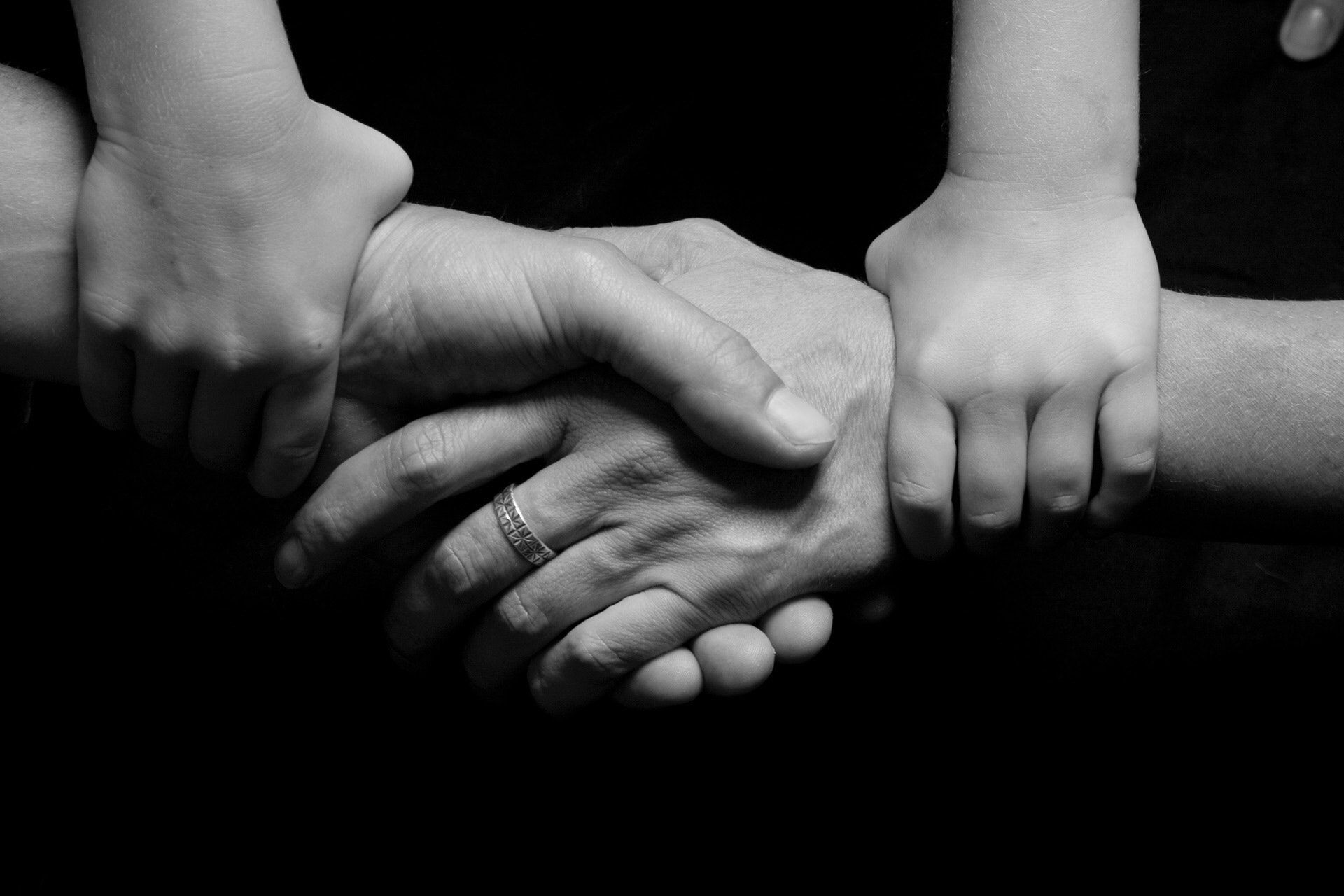 Three sets of hands clasped together: an adult's, a child's, and another adult's, in black and white.