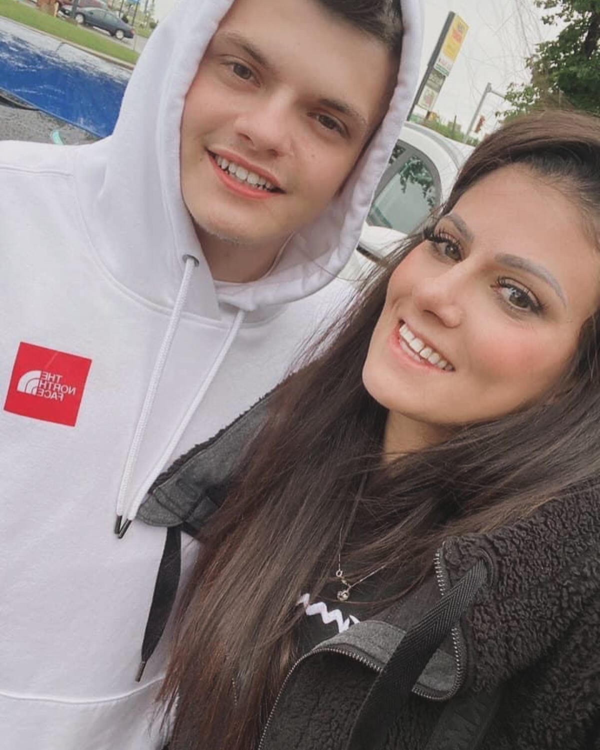 A man and a woman are posing for a picture together . the man is wearing a white hoodie.