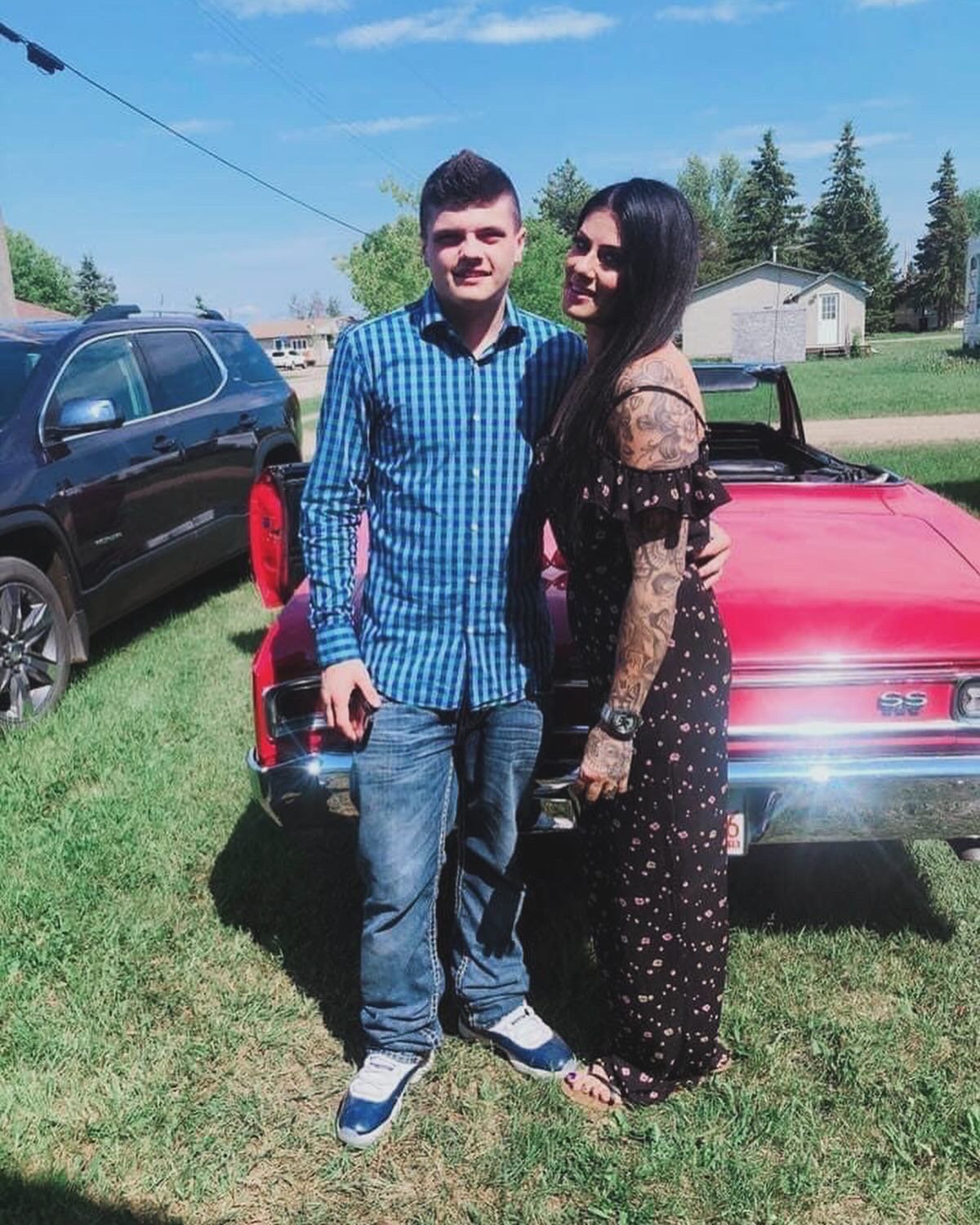 A man and a woman are posing for a picture in front of a red car.