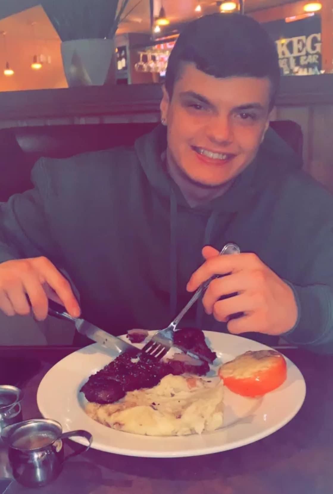 A young man is sitting at a table with a plate of food and a keg sign in the background