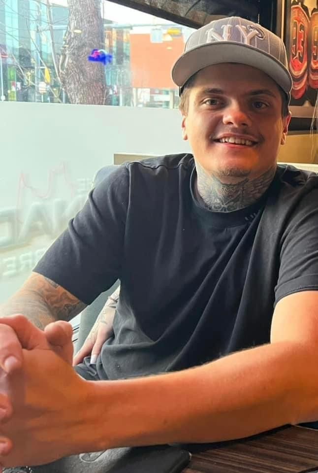A man wearing a hat and a black shirt is sitting at a table.