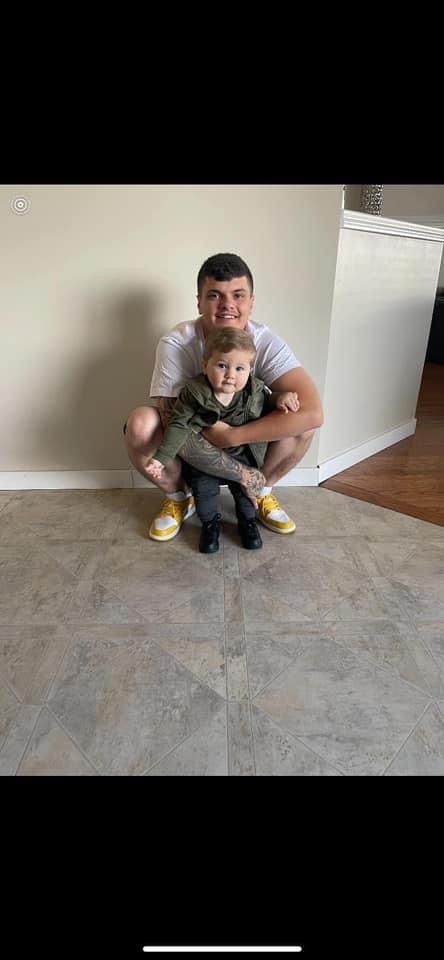 A man is kneeling down next to a little boy in a living room.