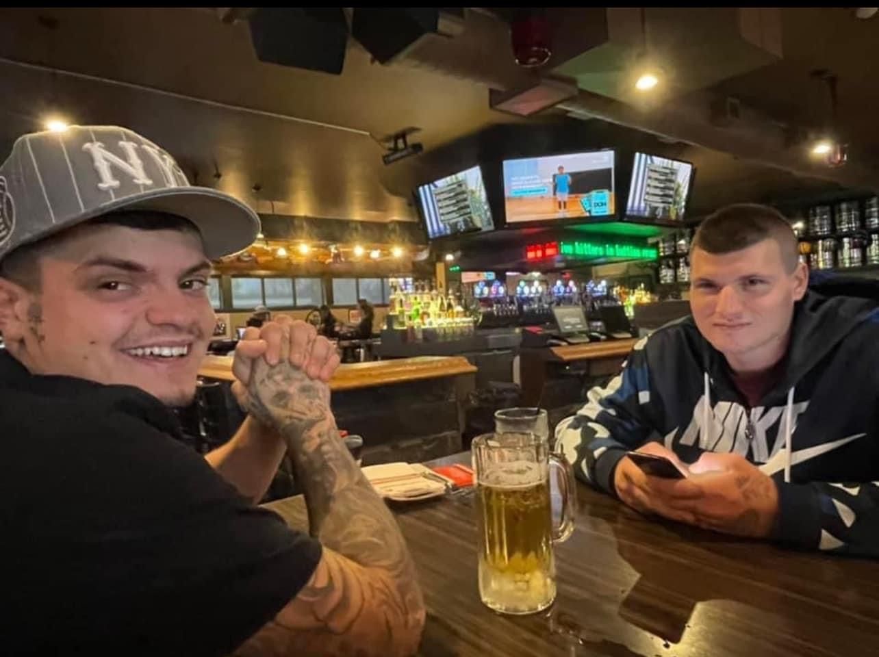 Two men are sitting at a bar drinking beer and looking at their phones.