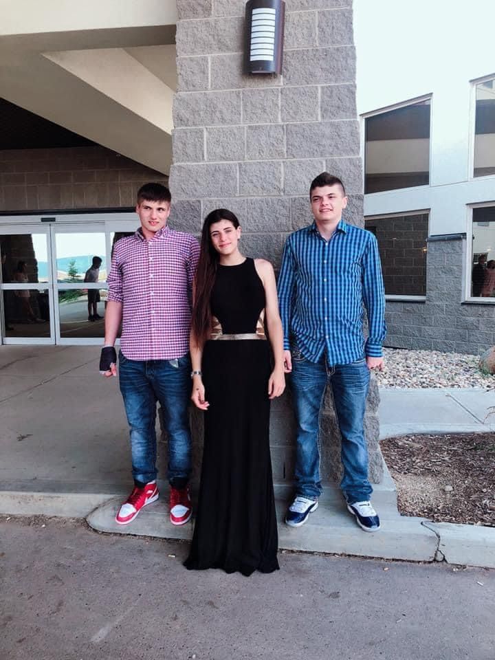 Two boys and a girl are posing for a picture in front of a building.