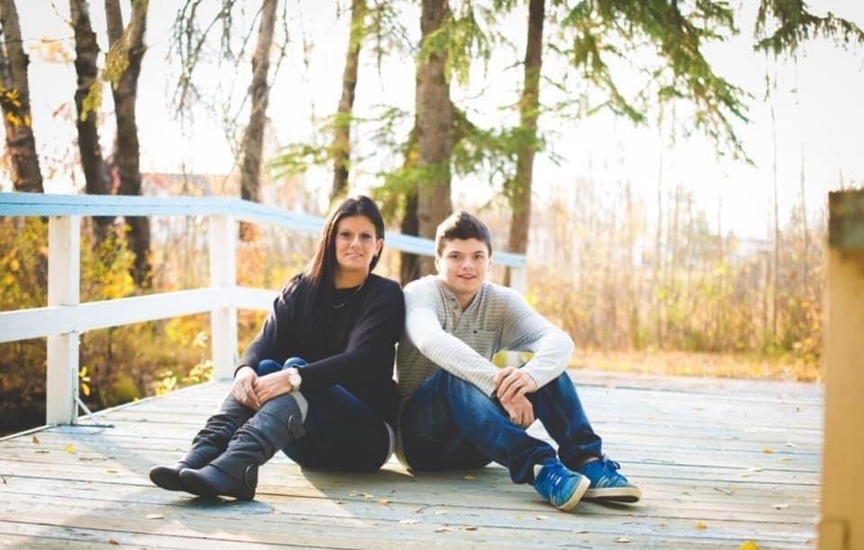 A woman and a boy are sitting on a wooden bridge.