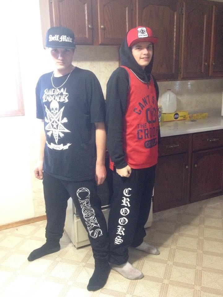 Two boys are standing next to each other in a kitchen one is wearing a black shirt with skulls on it