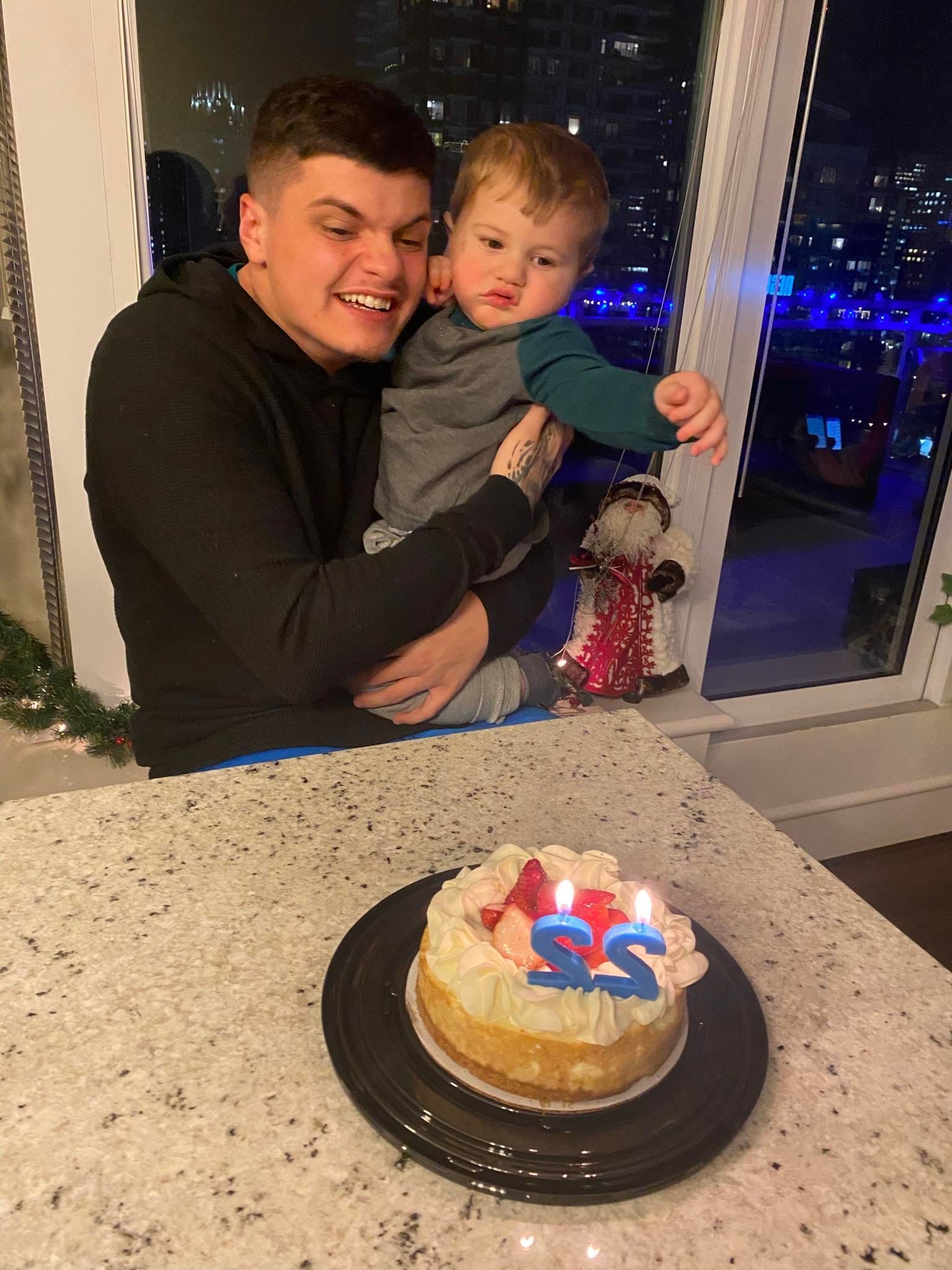 A man is holding a baby in front of a birthday cake.
