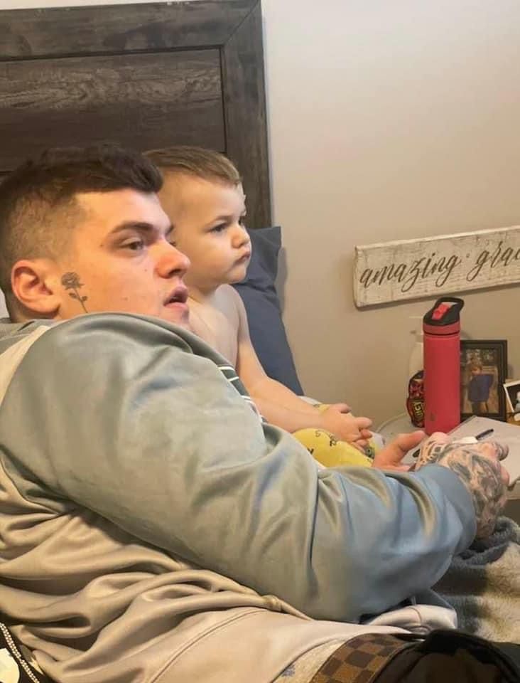 A man and a child are sitting on a bed playing a video game.