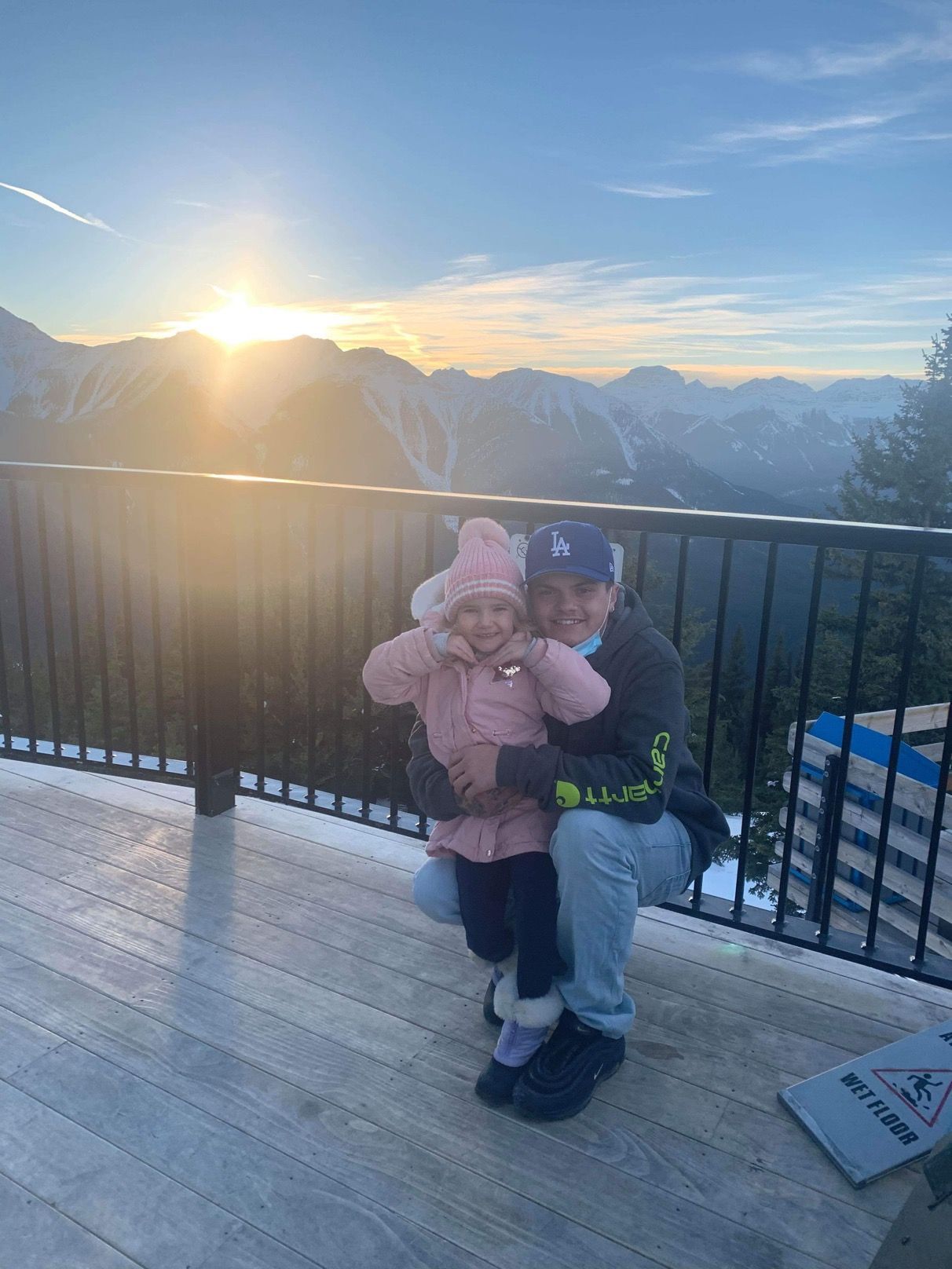 A man and a little girl are posing for a picture on a balcony overlooking a mountain range.