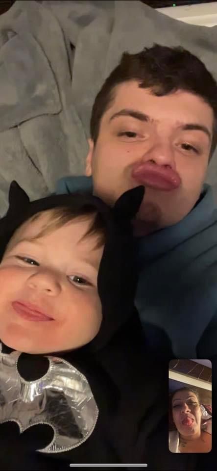 A man and a baby are having a video call . the baby is wearing a batman costume.