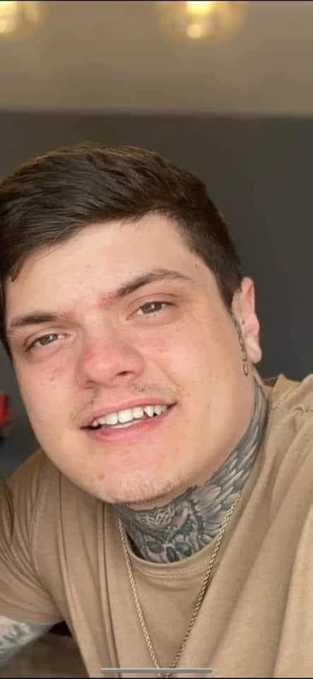 A young man with a tattoo on his neck is smiling for the camera.