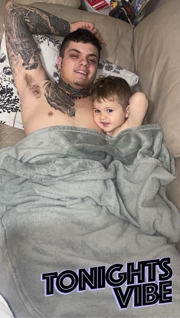 A man and a child are laying on a couch under a blanket.
