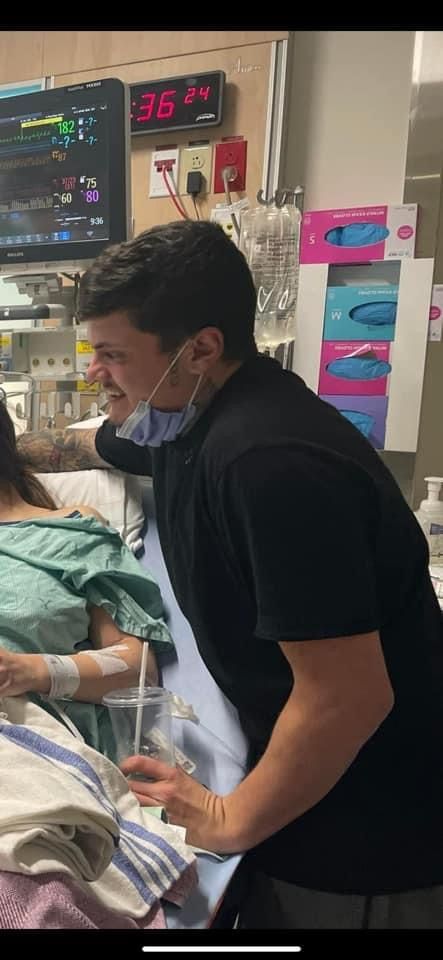 A man wearing a mask is standing next to a woman in a hospital bed.