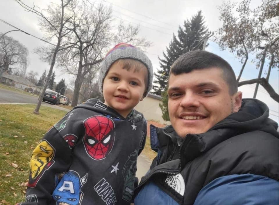 A man is holding a little boy who is wearing a spiderman sweatshirt.