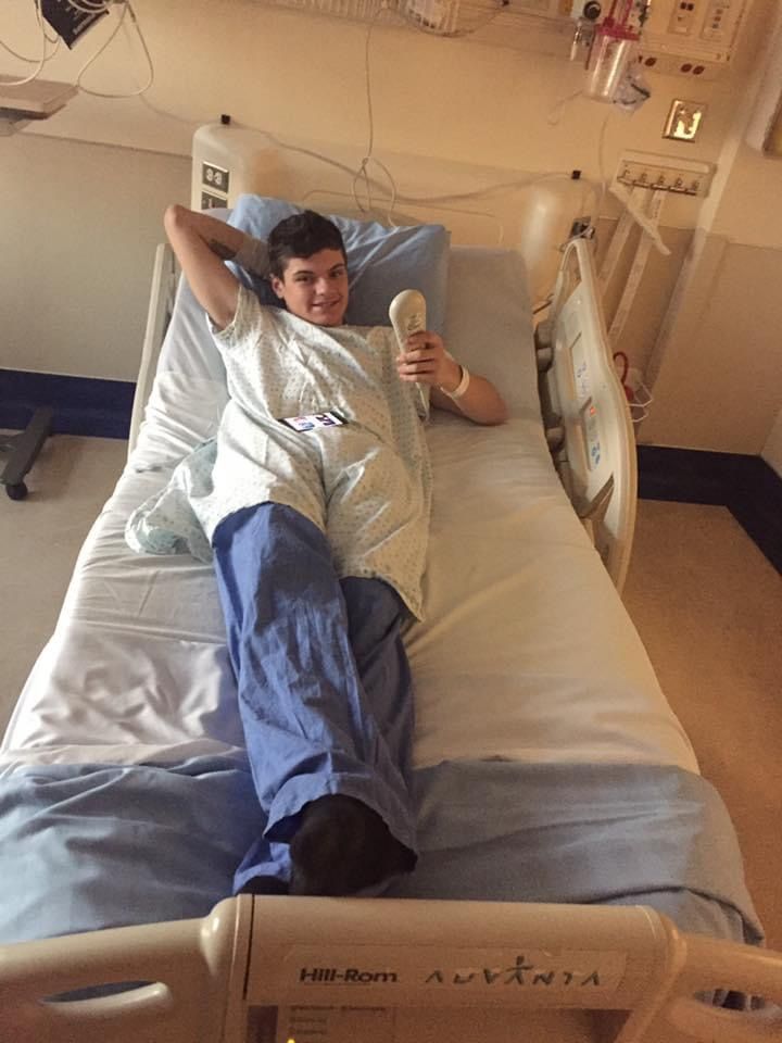 A young boy is laying in a hospital bed holding a cell phone.