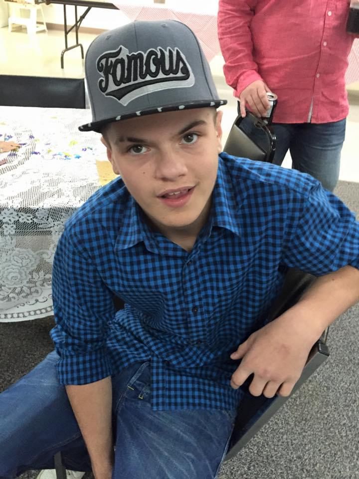 A young boy wearing a hat and a plaid shirt is sitting at a table.