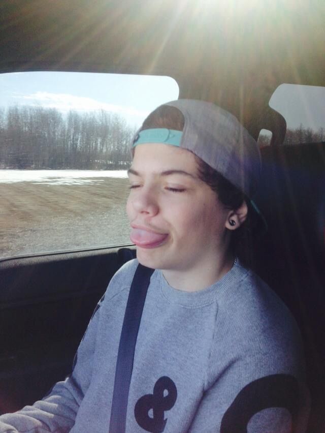 A boy wearing a hat and a sweater with the number 8 on it is sticking his tongue out