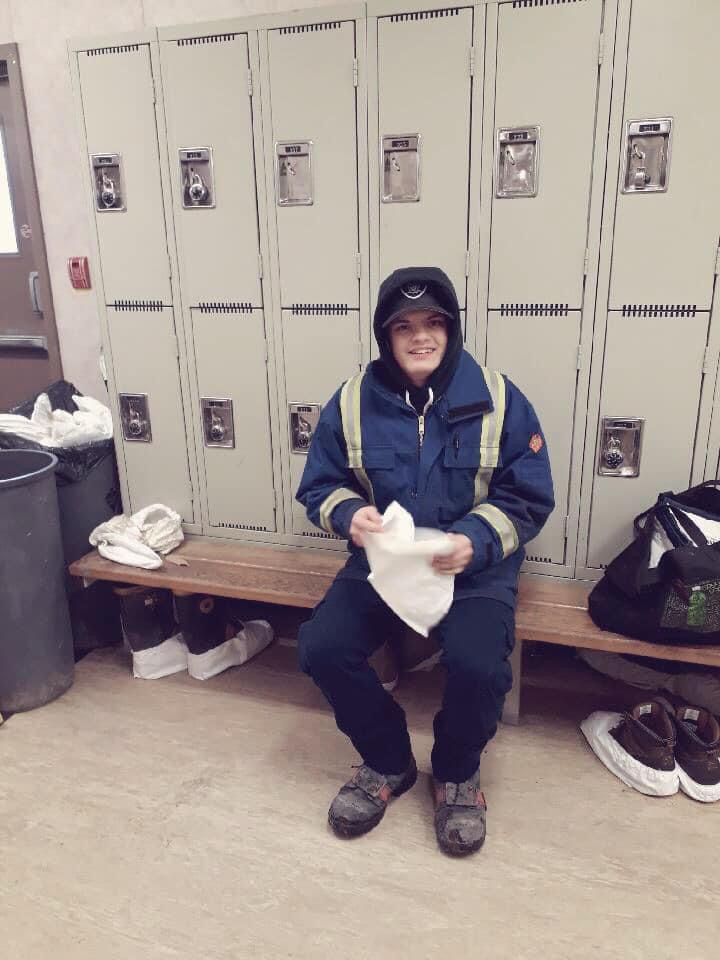 A man in a blue jacket is sitting on a bench in a locker room.
