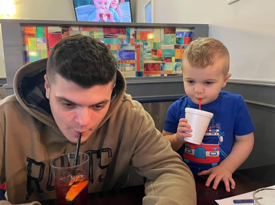 A man drinking through a straw next to a little boy