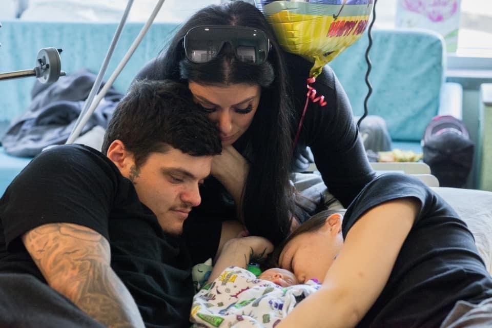 A man and a woman are holding a baby in a hospital bed.