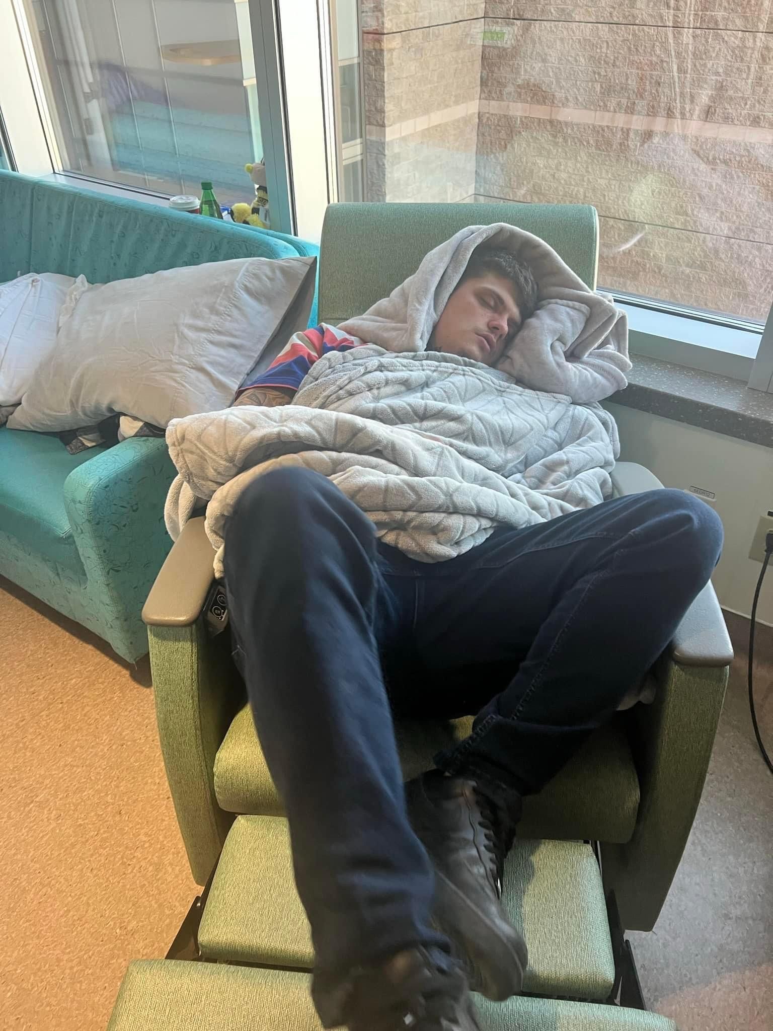 A man is sleeping in a chair wrapped in a blanket.