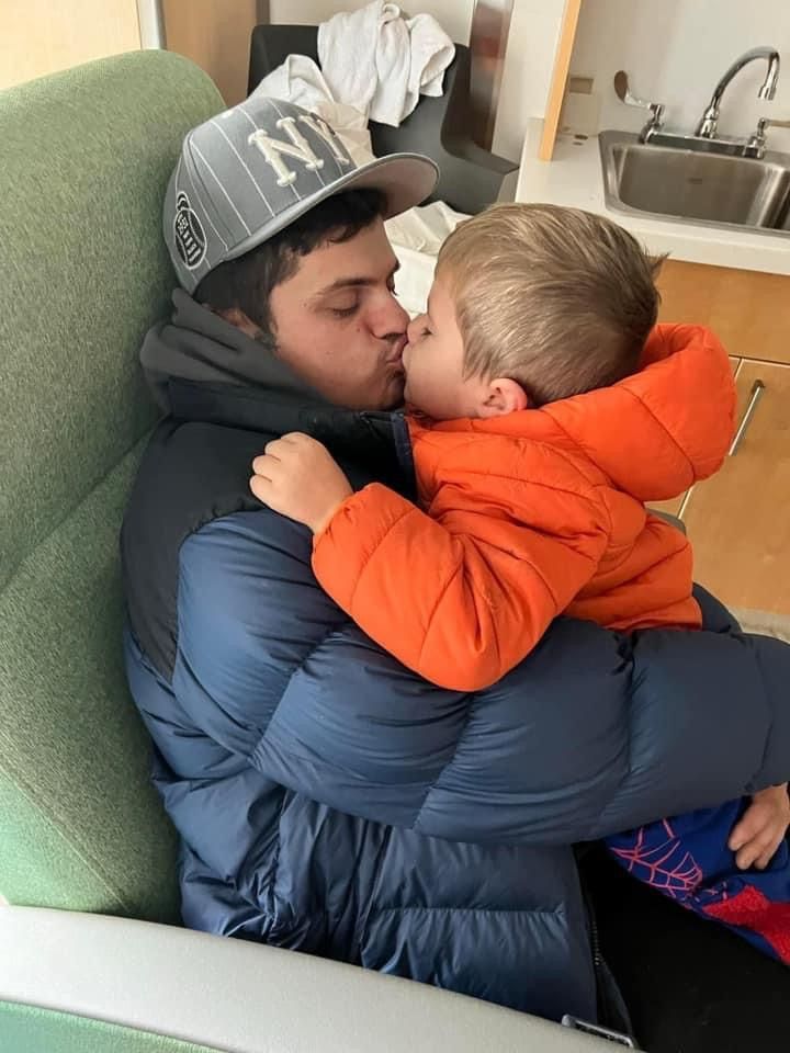 A man wearing a ny hat kisses a little boy on the cheek