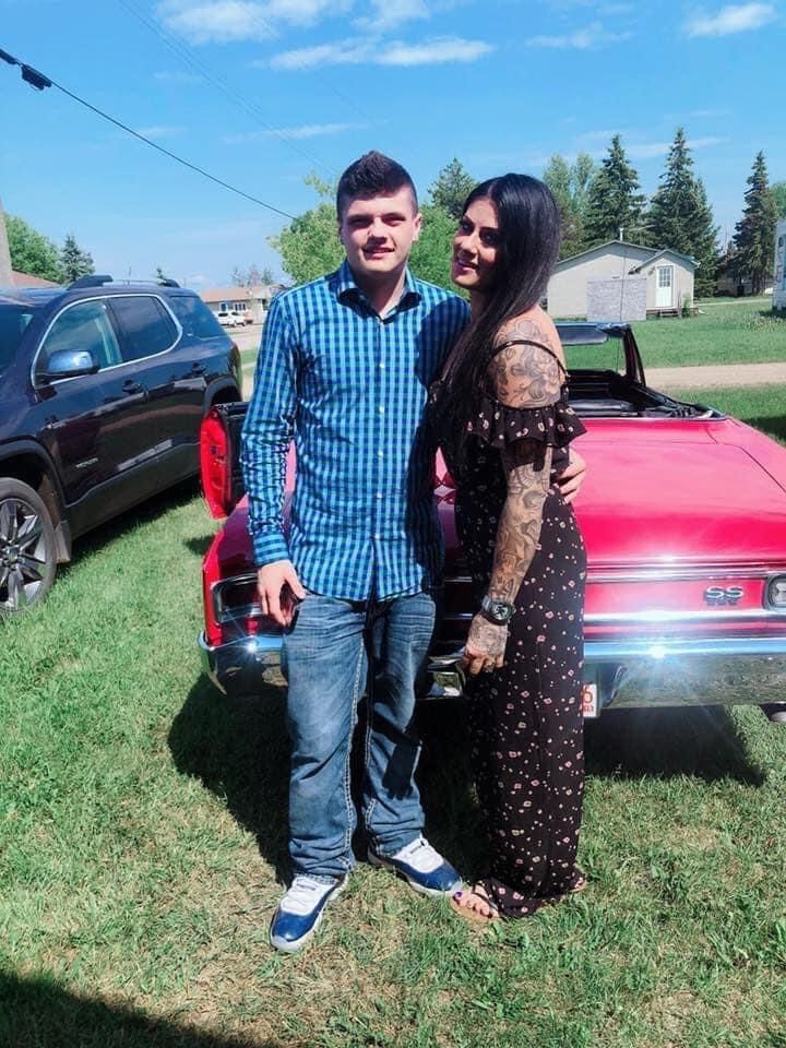 A man and a woman are posing for a picture in front of a red car.