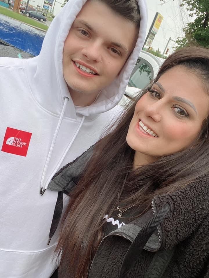A man and a woman are posing for a picture together . the man is wearing a white hoodie.