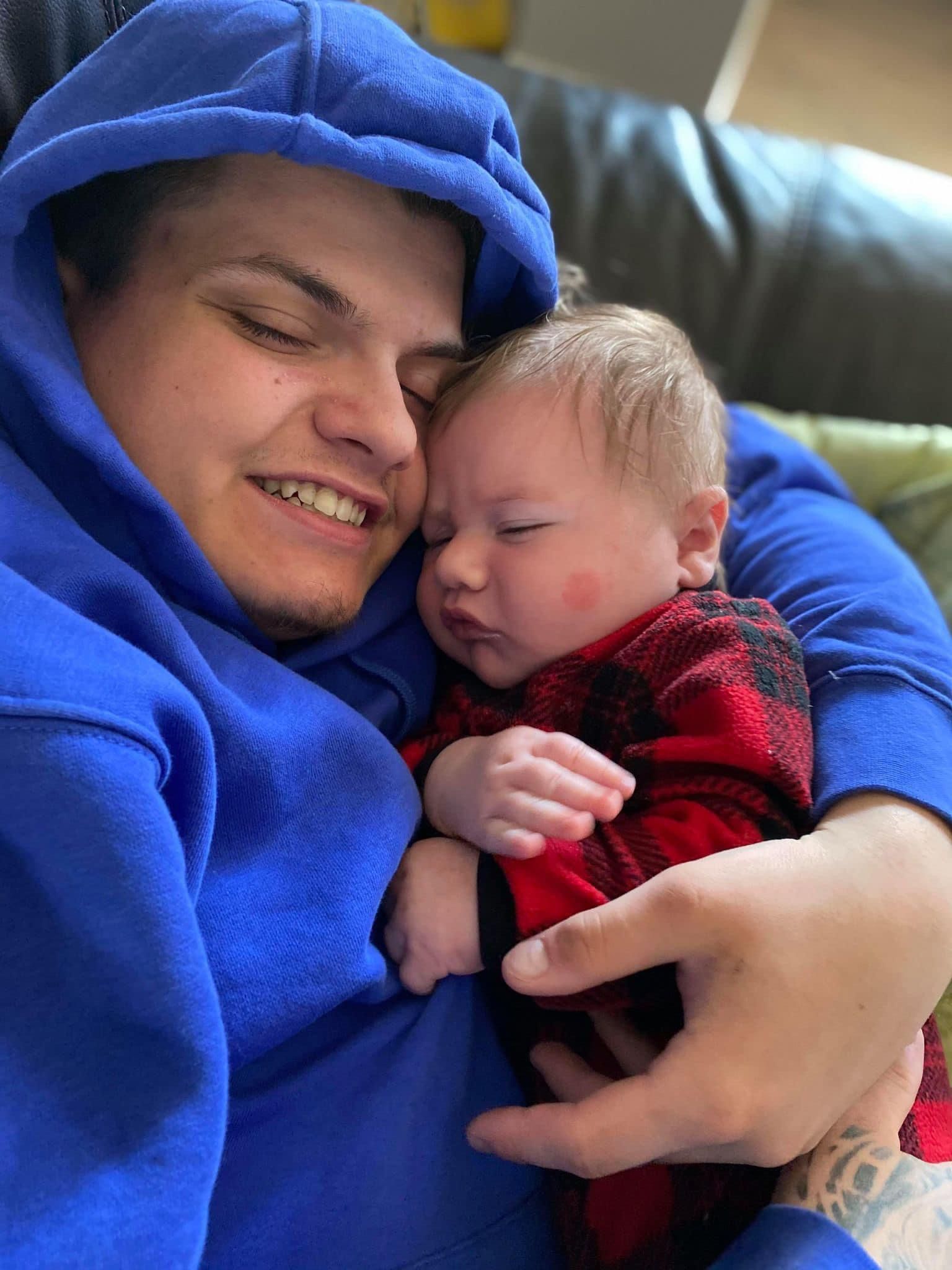 A man in a blue hoodie is holding a baby in his arms.