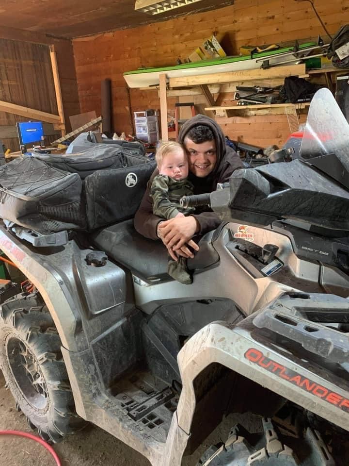 A man is holding a baby while sitting on a four wheeler.