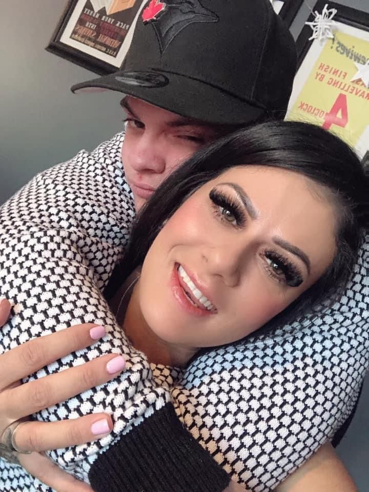 A man wearing a hat is hugging a woman who is smiling