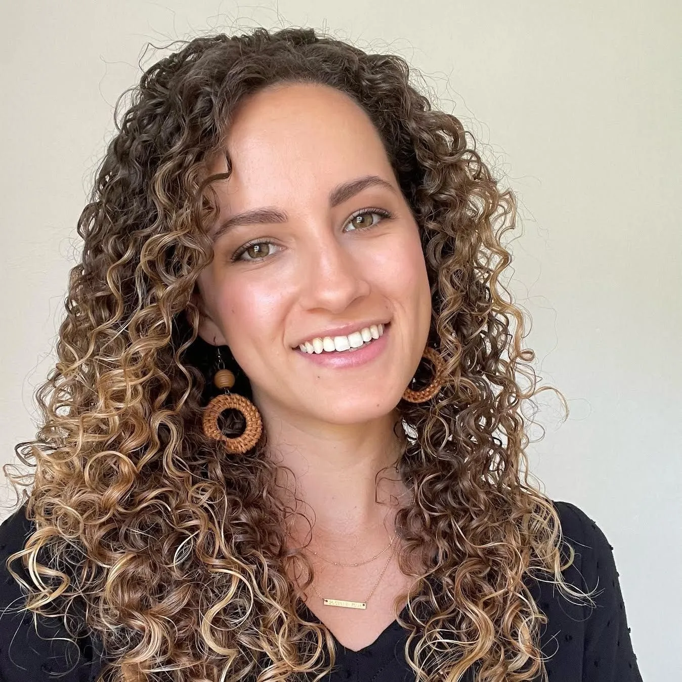A woman with curly hair and earrings is smiling for the camera.