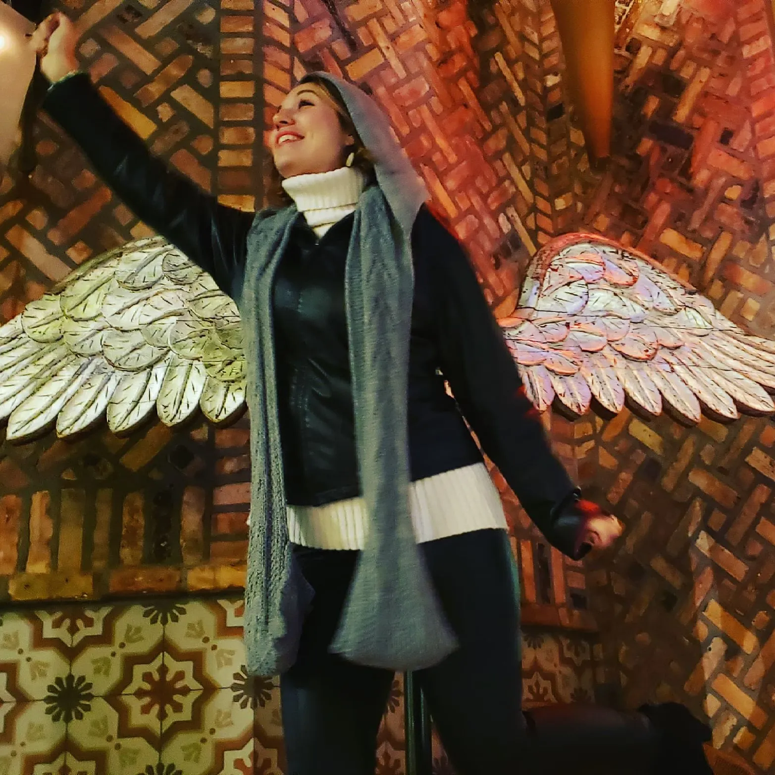 A woman wearing a scarf is standing in front of a wall with angel wings on it