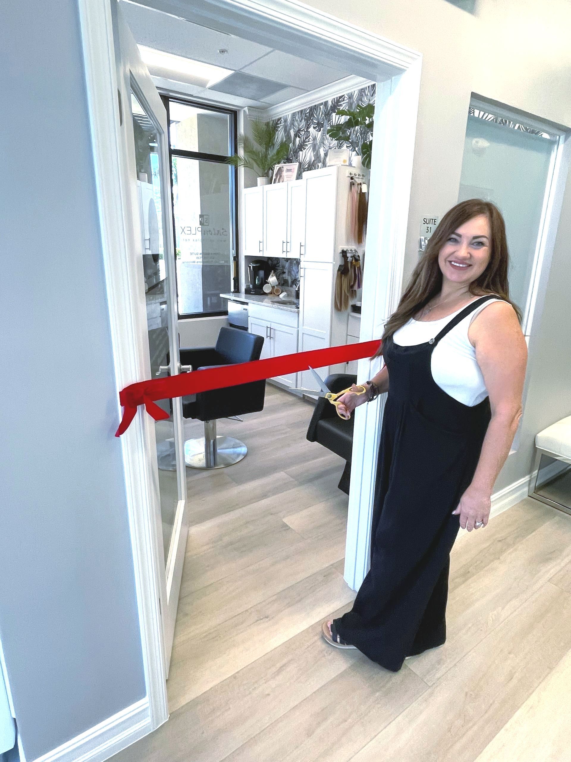 A woman with brown hair is smiling while cutting a ribbon.