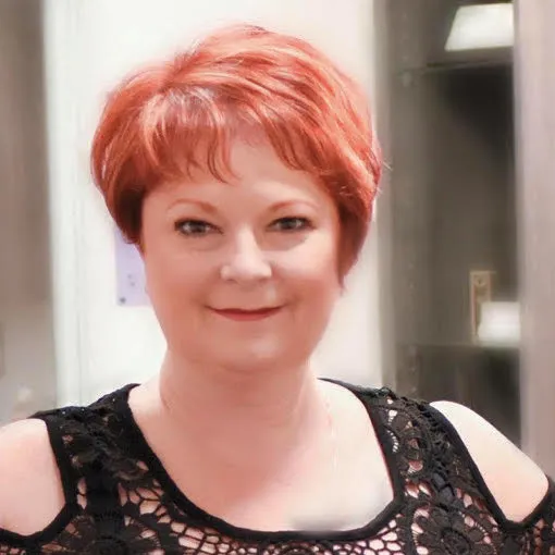 A woman with red hair is wearing a black lace top and smiling.