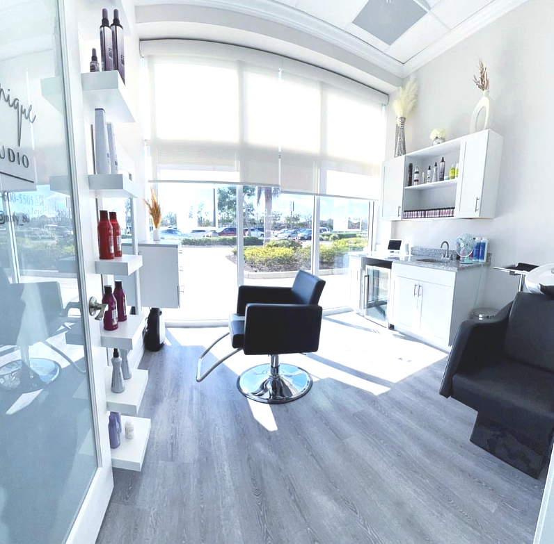 A hair salon with a chair , sink , and windows.